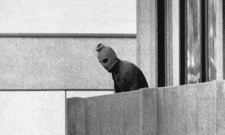 A member of the Arab commando group wearing a balaclava looks over a balcony 