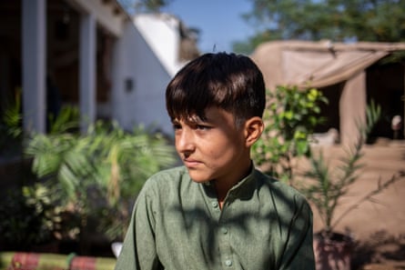 A young boy in a green button-up shirt sits outside a house in the sunshine.