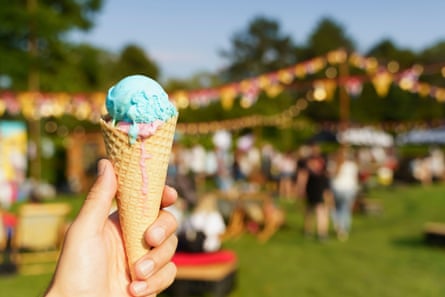 A hand holding an ice-cream cone against a blurred background of a summer fair