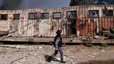 Getty Images A member of Israeli security forces walks past a damaged building at the site of a rocket strike in Kiryat Shmona in northern Israel on 24 September