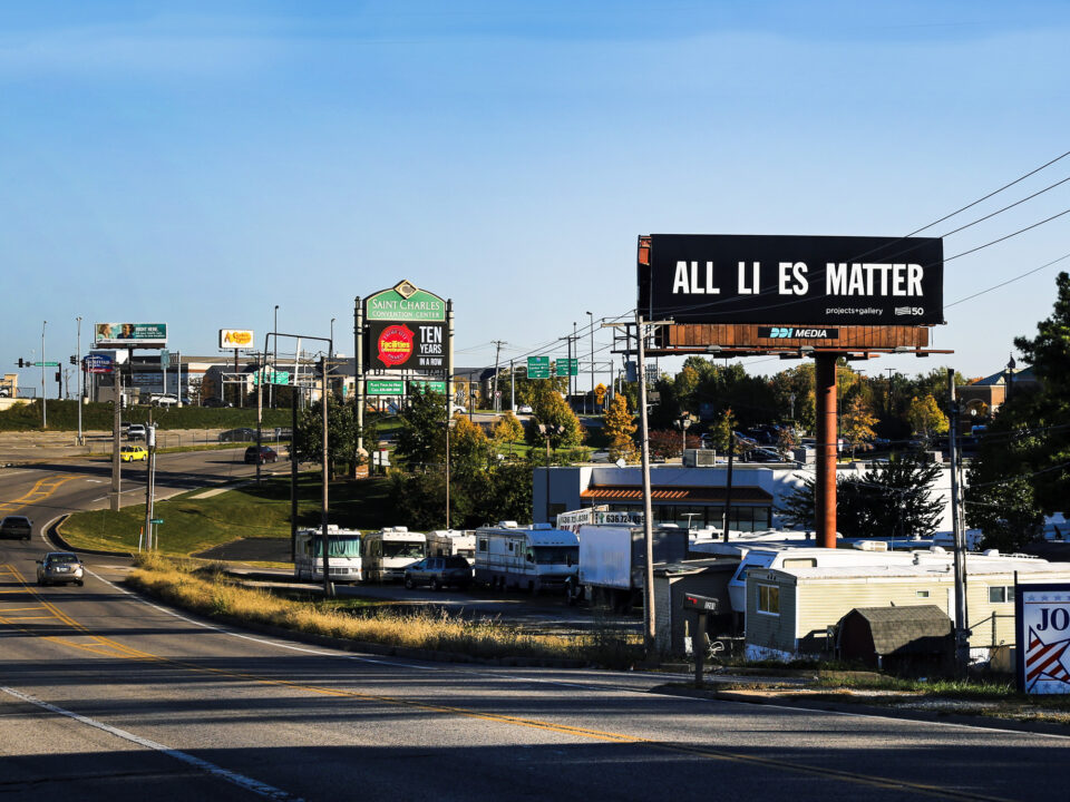 a black billboard with white text reading, "ALL LIES MATTER"