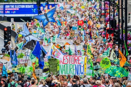 Thousands of people march along a city street holding banners with slogans including ‘Restore Nature Now!’ and flags in the shape of butterflies.