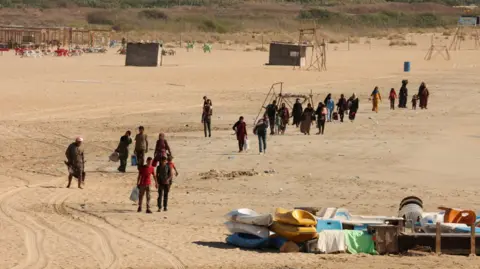 Reuters People carry their belongings across a beach as they leave Tyre - one of the southern Lebanon cities hit on Monday