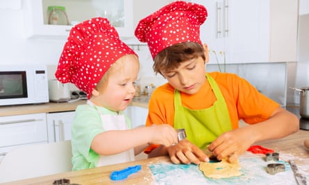 Two children making pastry in kitchen wearing chefs' hats in red