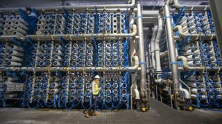 A woman walks along a wall stacked with tubes in a water desalination plant