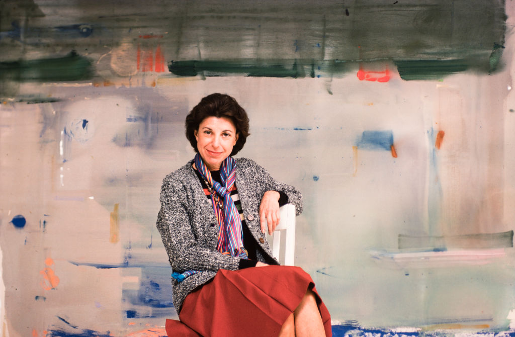 A woman sits in front of an an abstract painting.