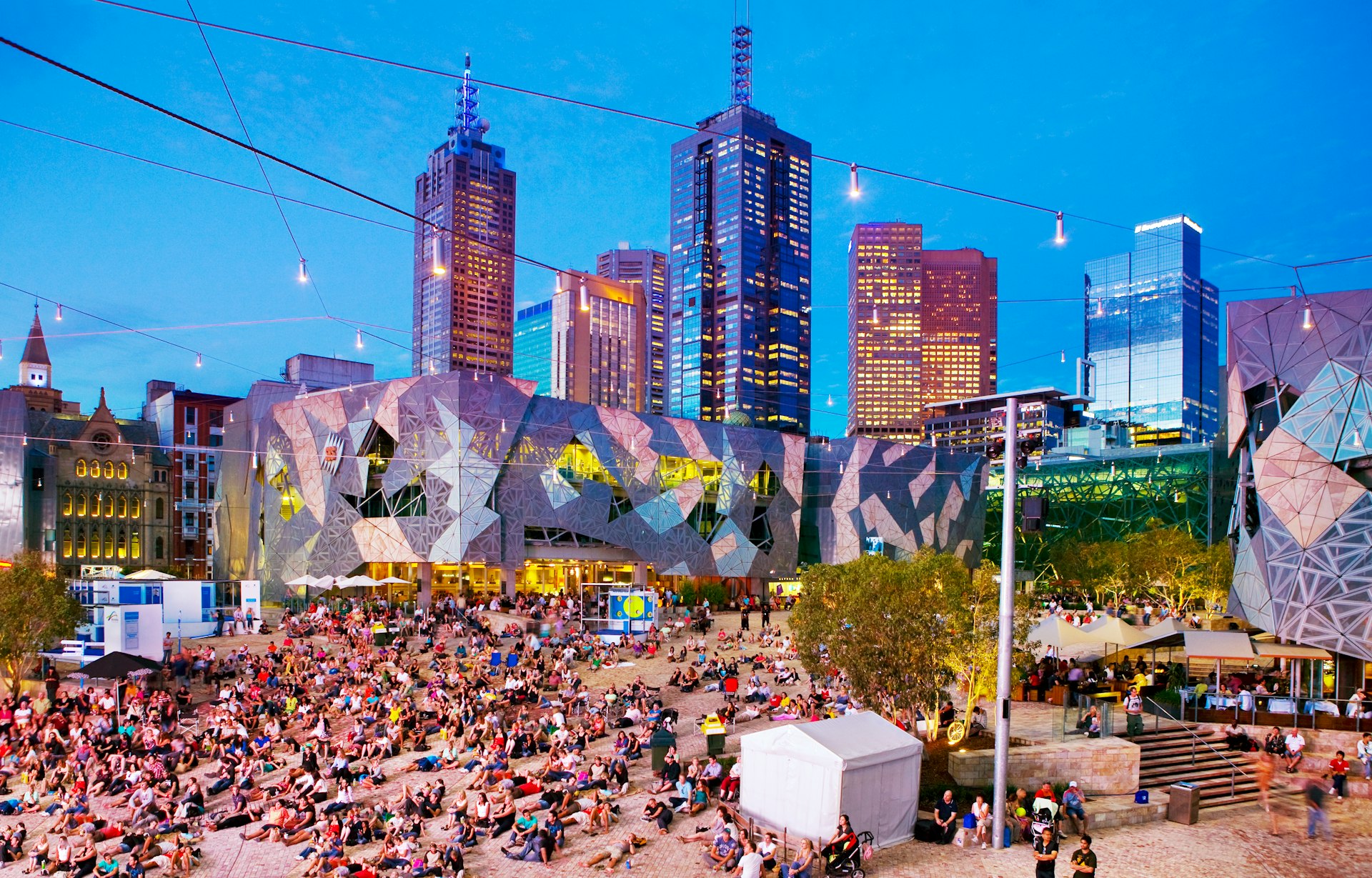 People relax in a city square lit up at dusk