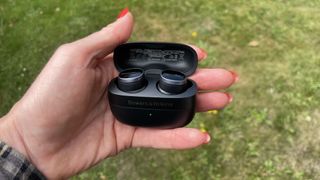 Bowers & Wilkins Pi8 earbuds, held in a hand on grassy background