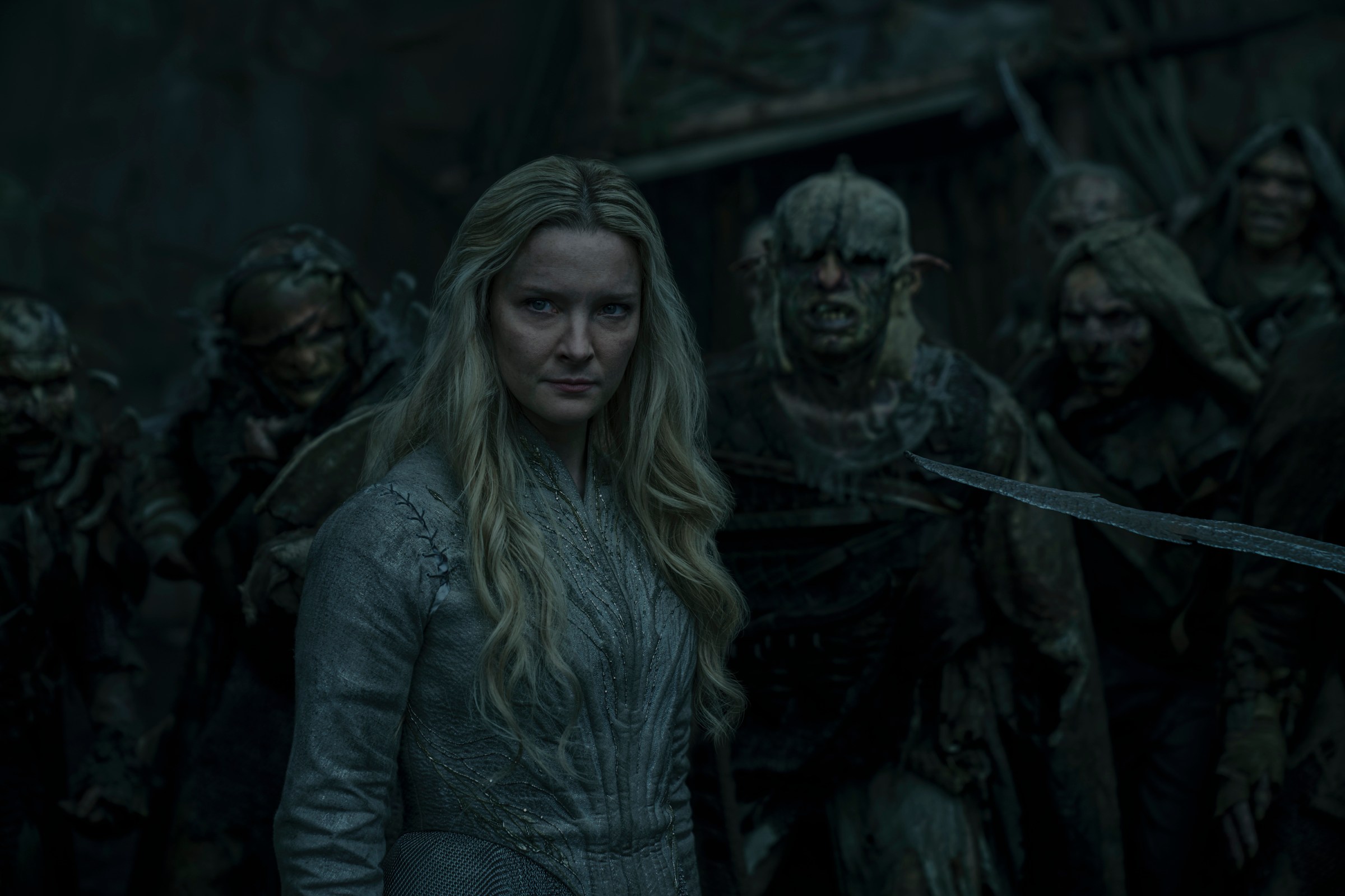 Morfydd Clark as Galadriel in Lord of the Rings: The Rings of Power standing in full armor in front of a group of orcs