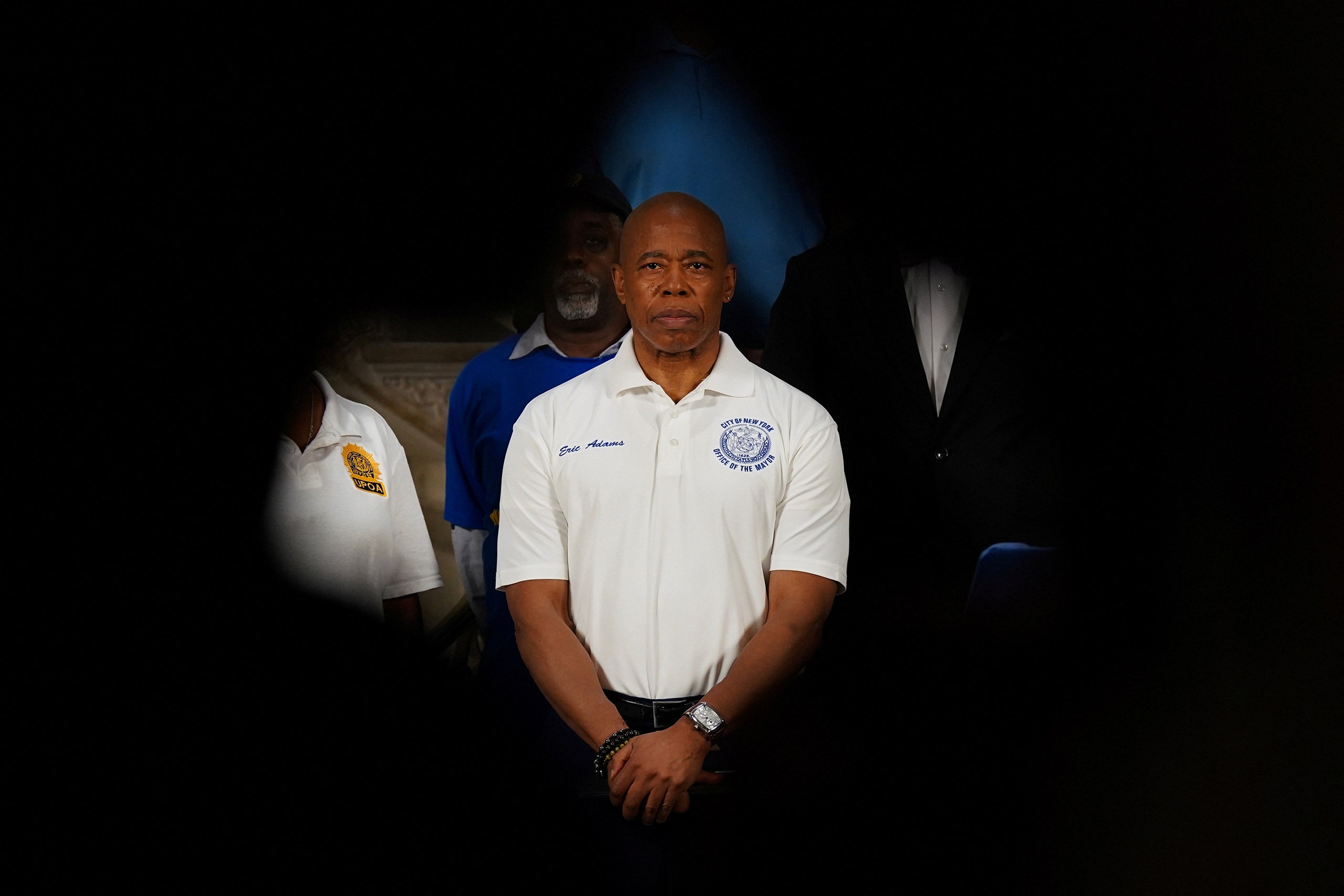 New York City Mayor Eric Adams at a press conference wearing black pants and a white polo shirt.