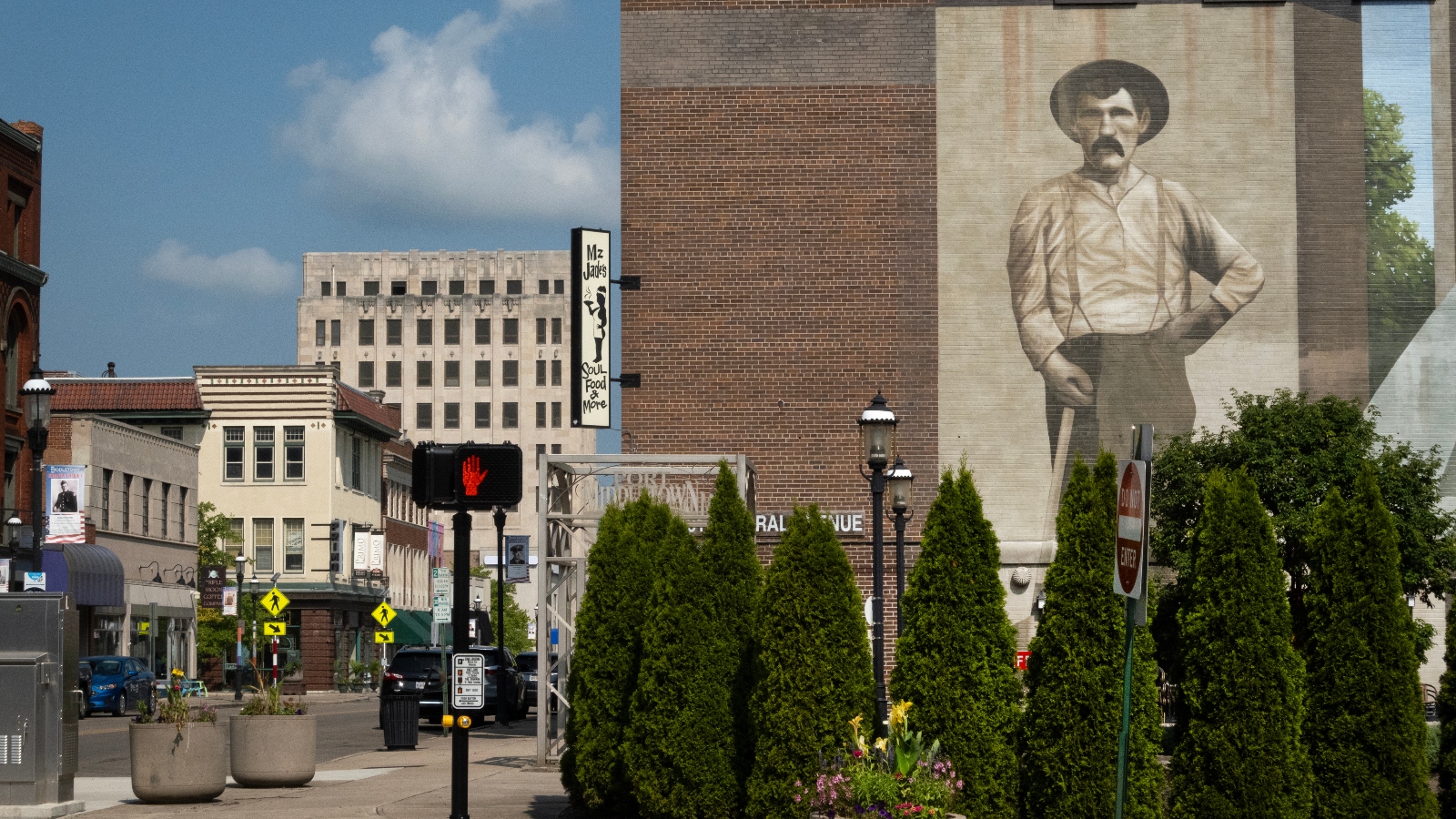 A mural of an old timey man in a hat stands on a brick building on a small town street