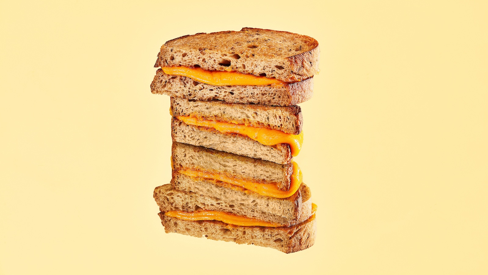 Two halves of a grilled cheese sandwich are stacked on top of each other against a pale yellow background