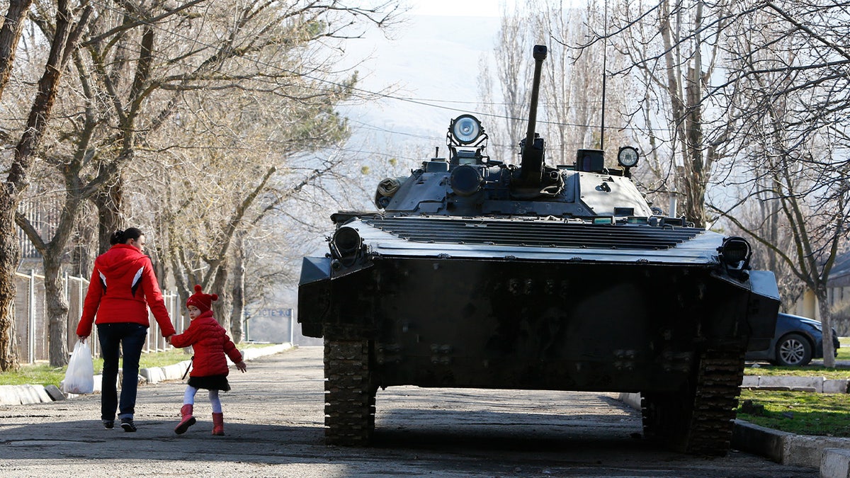 A woman and a child walk past an armoured vehicle at a military base in Perevalnoye, near the Crimean city of Simferopol March 21, 2014. 