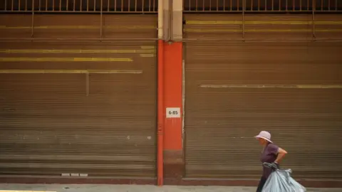 Xiqing Wang/BBC A woman walks past closed shops in Ruili 