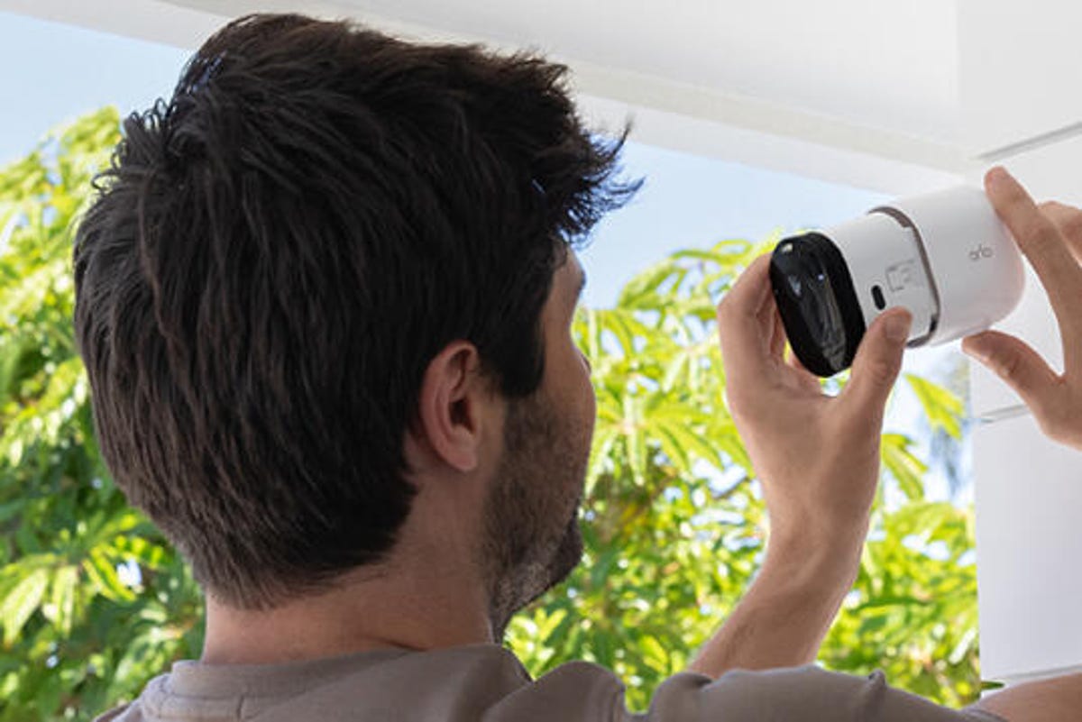 A man installs an Arlo Pro cam on white outdoor siding.