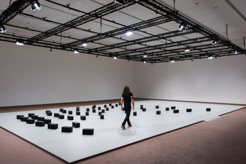 a person walks through an installation with black rectangular blocks on the gallery floor