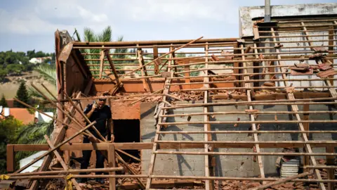 Reuters An Israeli policeman walks on a roof of a house in northern Israel that was hit by a rocket fired from Lebanon by Hezbollah (23 September 2024)