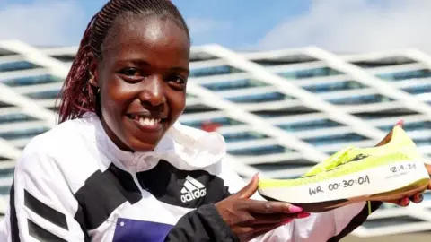 Getty Images Agnes Jebet Tirop holding a running shoe with the following written on the side by hand: WR 00:30:01