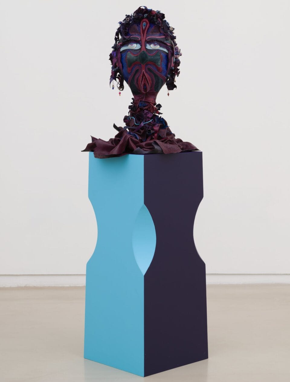 a purple, blue, green, and red fabric bust on a blue and purple pedestal. the figure has wide eyes and earrings