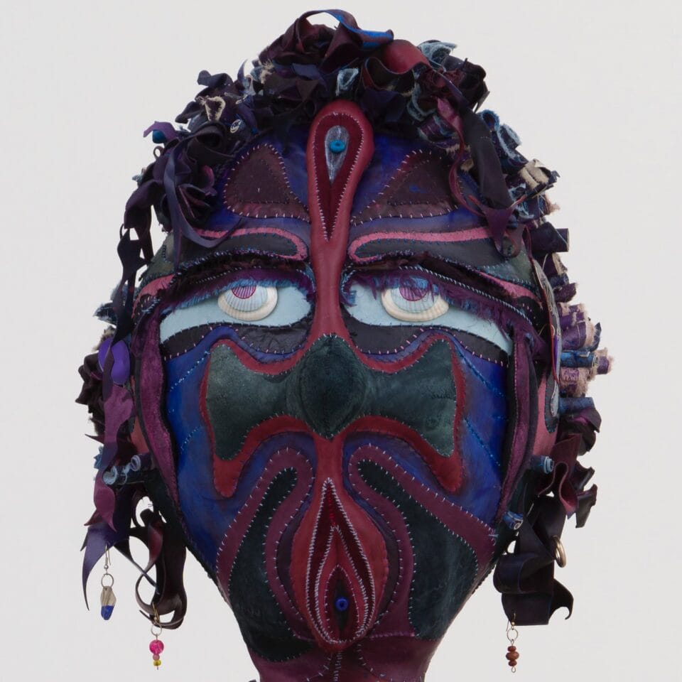 a detail of a purple, blue, green, and red fabric bust. the figure has wide eyes and earrings