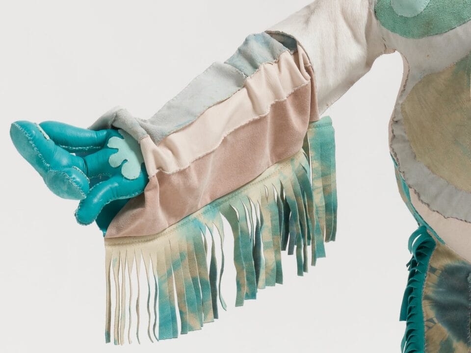 a detail image of a blue fabric hand with white and beige sleeve with tassels