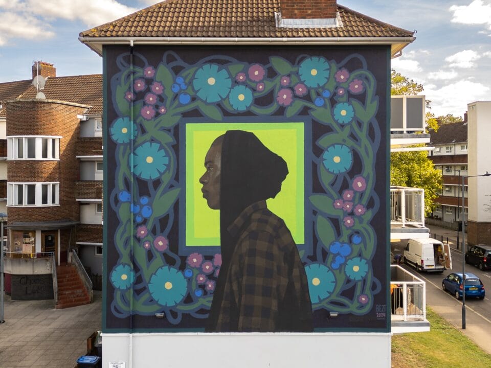 a mural of the profile of a black man in a hoodie and plaid shirt surrounded by blue and pink flowers