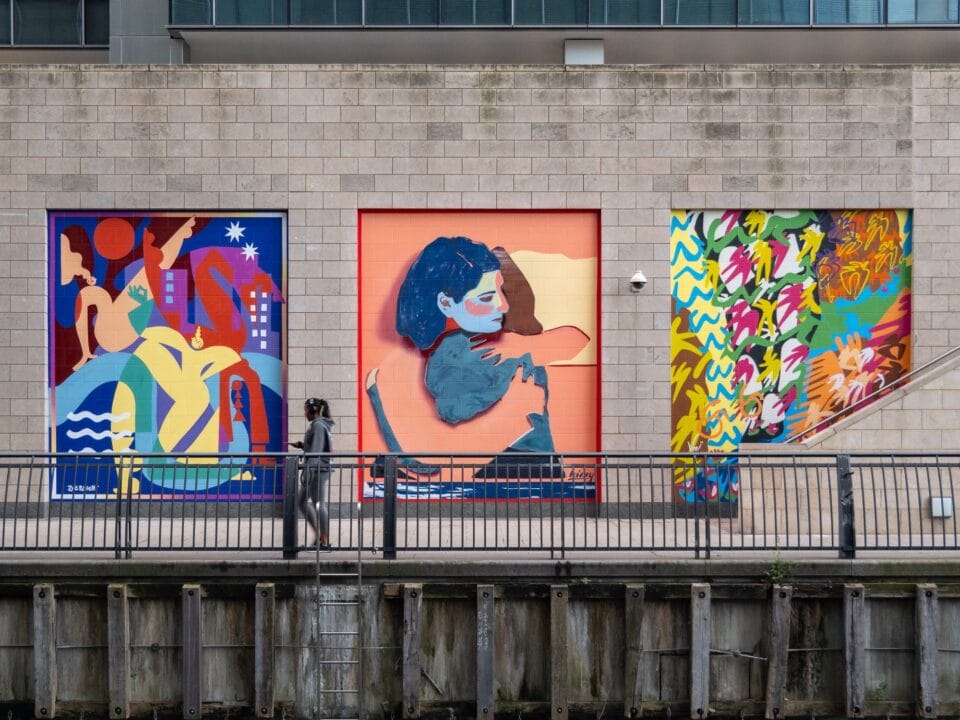 three colorful murals, the middle figurative, in a brick wall along a rail