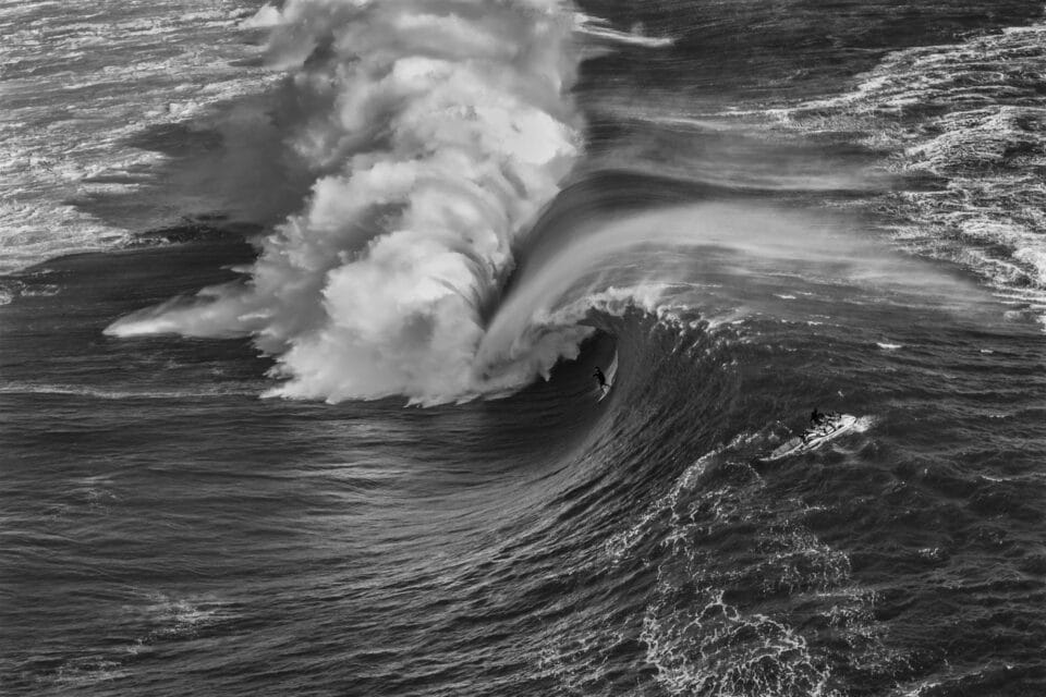 in a black and white photo, a large barreling wave begins to crash down on itself