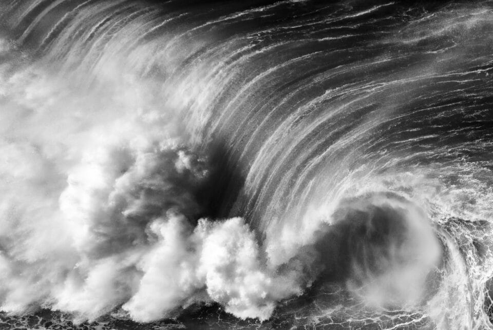 in a black and white photo, a large barreling wave begins to crash down on itself