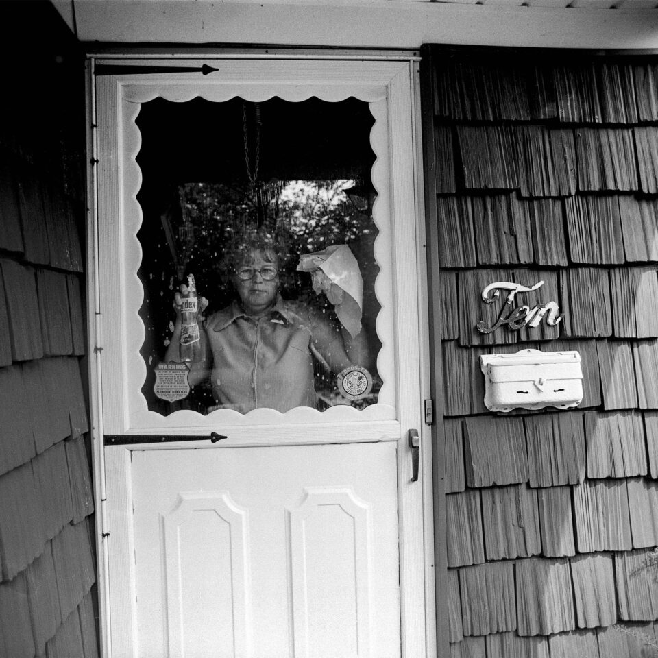 a black and white photograph of a woman cleaning the glass through a door