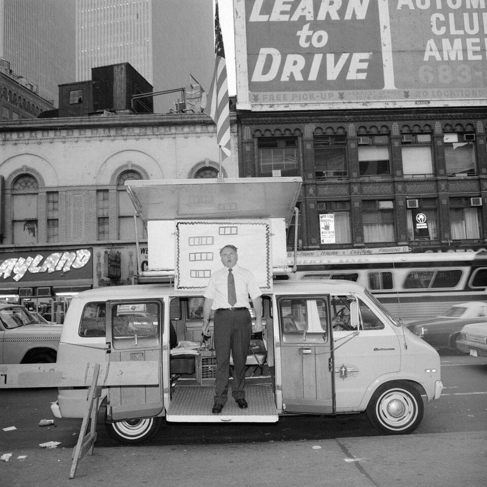 a black and white photograph of a man standing in the doorway of a news van parked on the city street