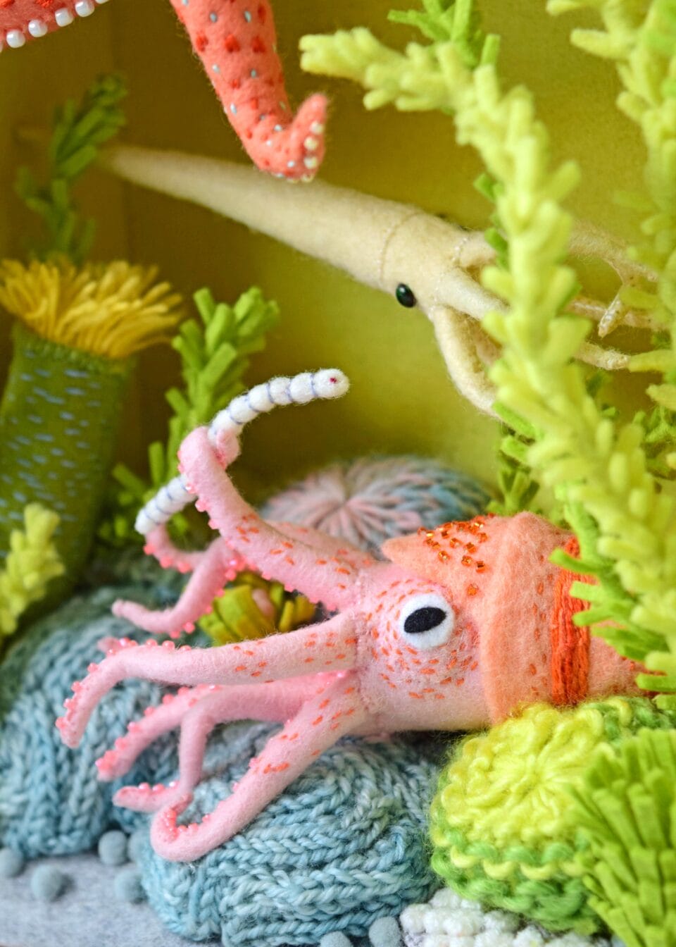 a detail image of a pink squid holding a worm with blue crochet below it