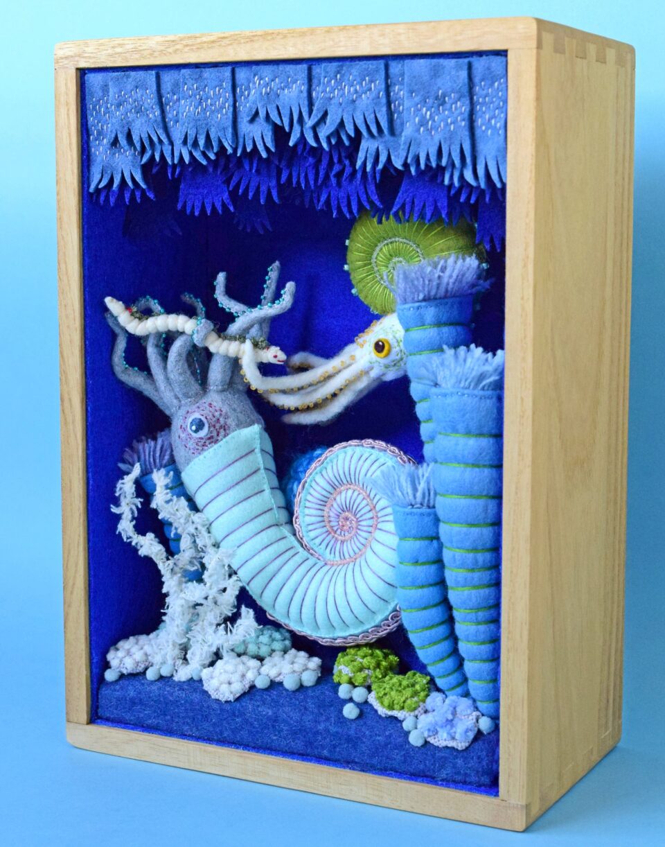 a diorama in a wooden box of a plush blue and green ammonite and other marine creatures