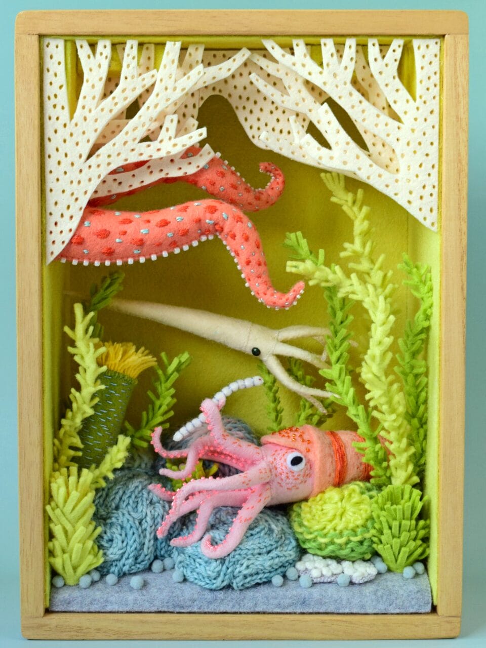 a diorama in a wooden box of a plush pink squid, white squid, and other marine creatures