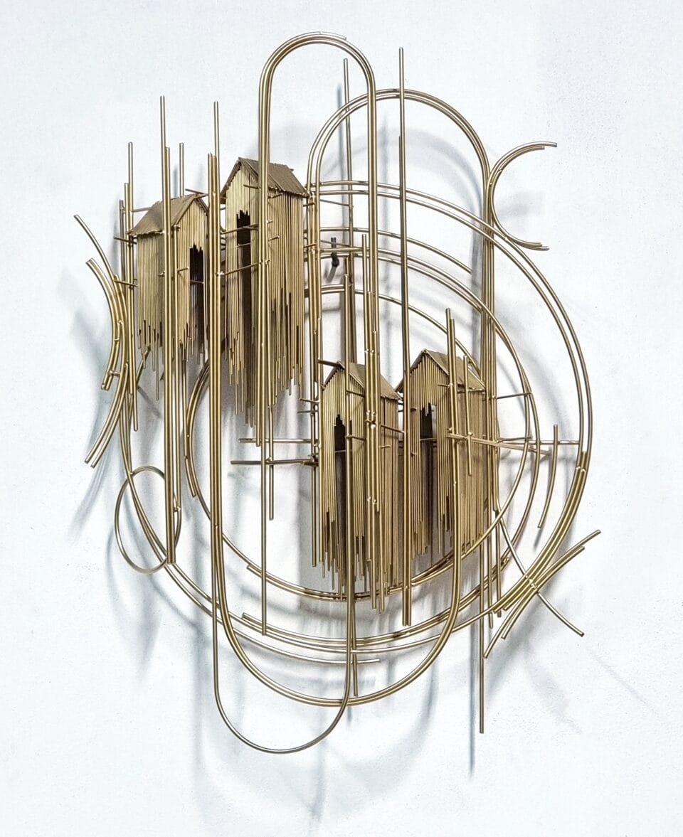 a wall sculpture made of numerous pieces of steel wire assembled in an abstract composition of house-like forms on gold scaffolding