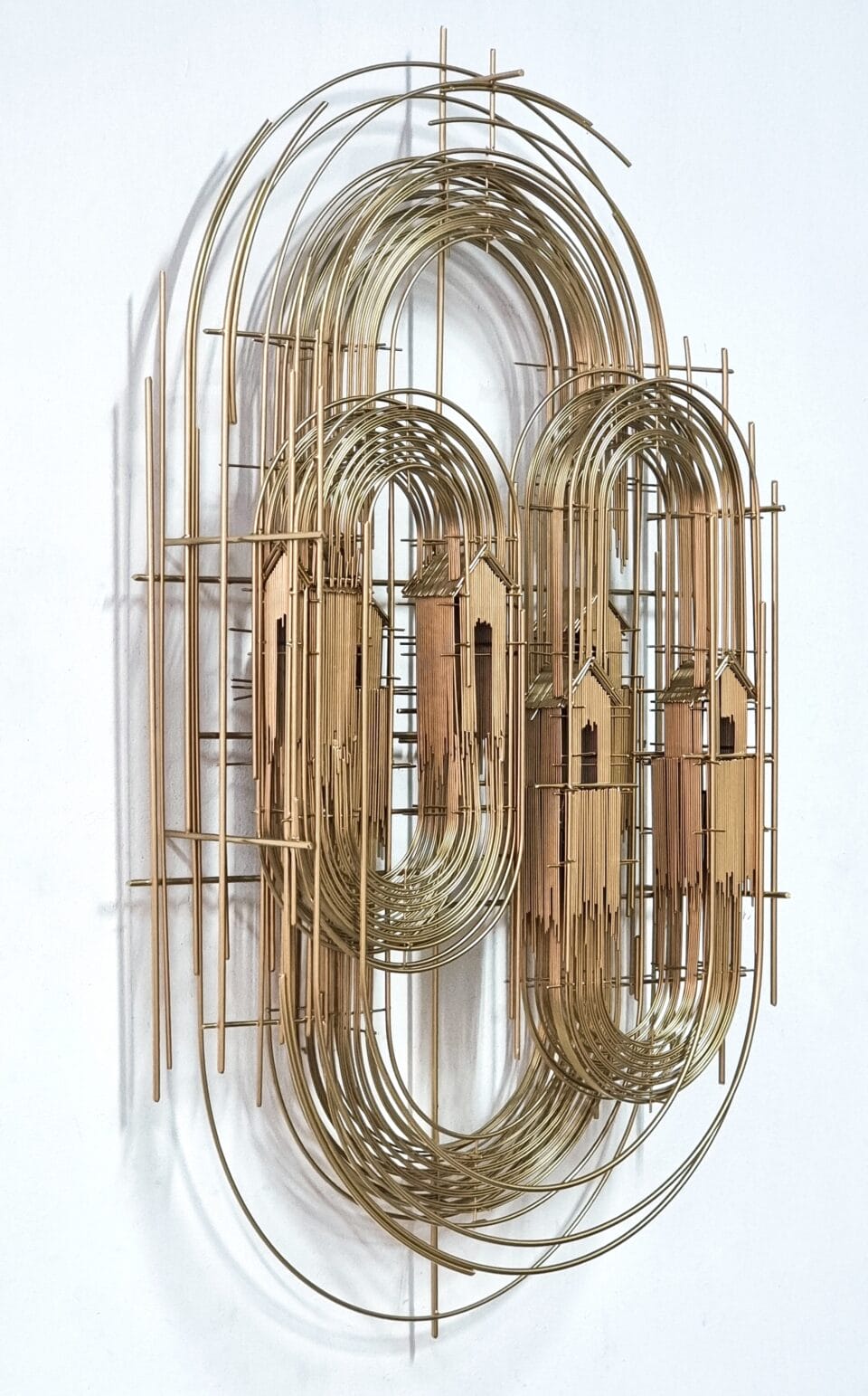 a wall sculpture made of numerous pieces of steel wire assembled in an abstract composition of house-like forms on gold scaffolding