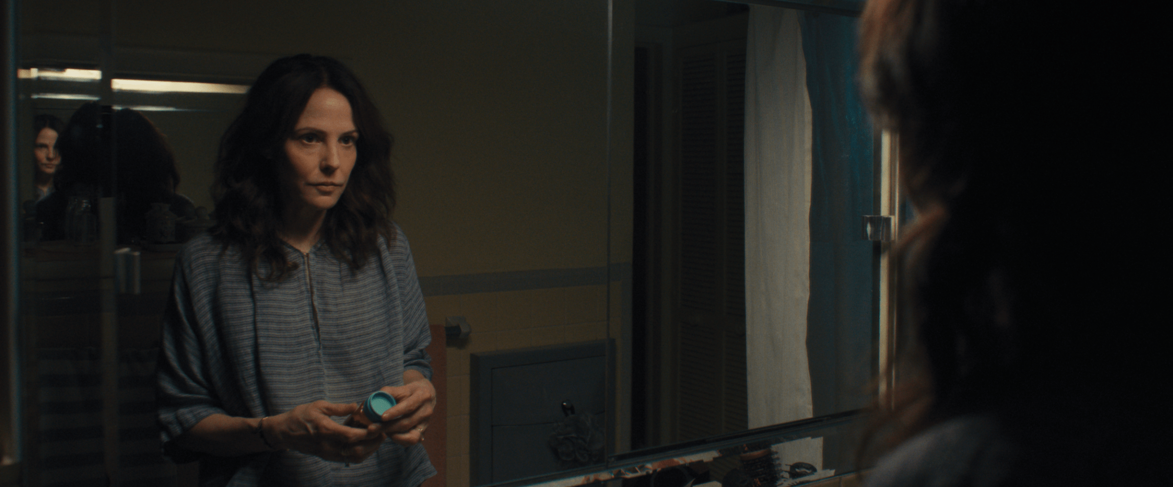 Mary-Louise Parker handles a bottle of pills and looks into a mirror in Omni Loop.