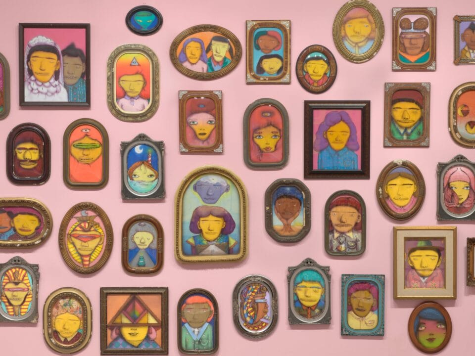 a detail image of a collection of small framed portraits of yellow figures on a pink wall