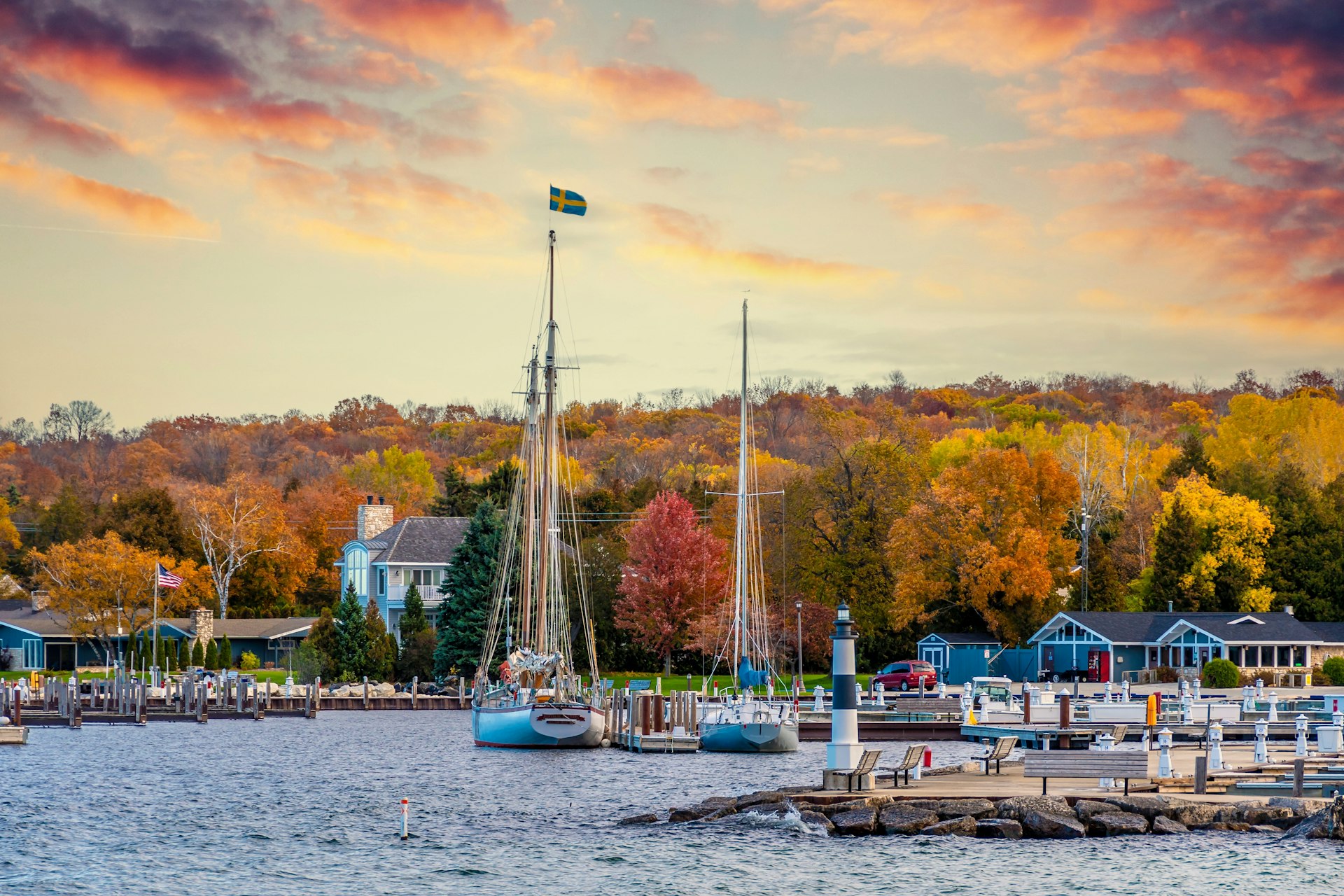 A small harbor town with sail boats moored in the dock. Trees are all golden marking autumn months