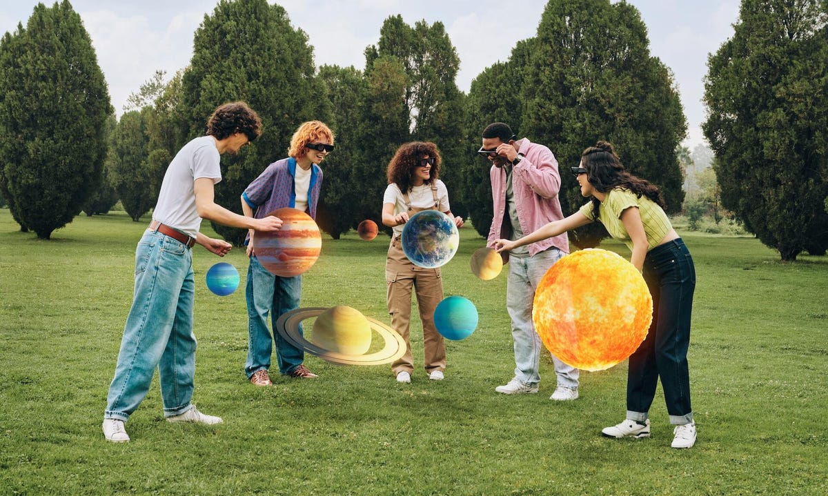 A group of people outdoors looking at a virtual solar system with glasses on