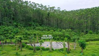 An aerial image of a tropical landscape with a small paved clearing and a sign that reads "TIKTIK NOL NUSANTARA"