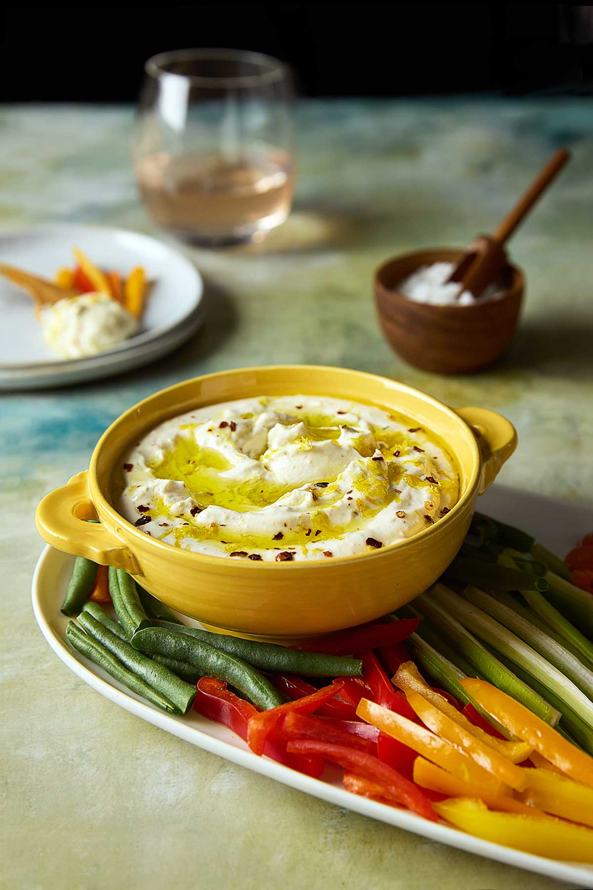 A bowl of whipped feta dip topped with oil and lemon zest on a platter of raw vegetables.