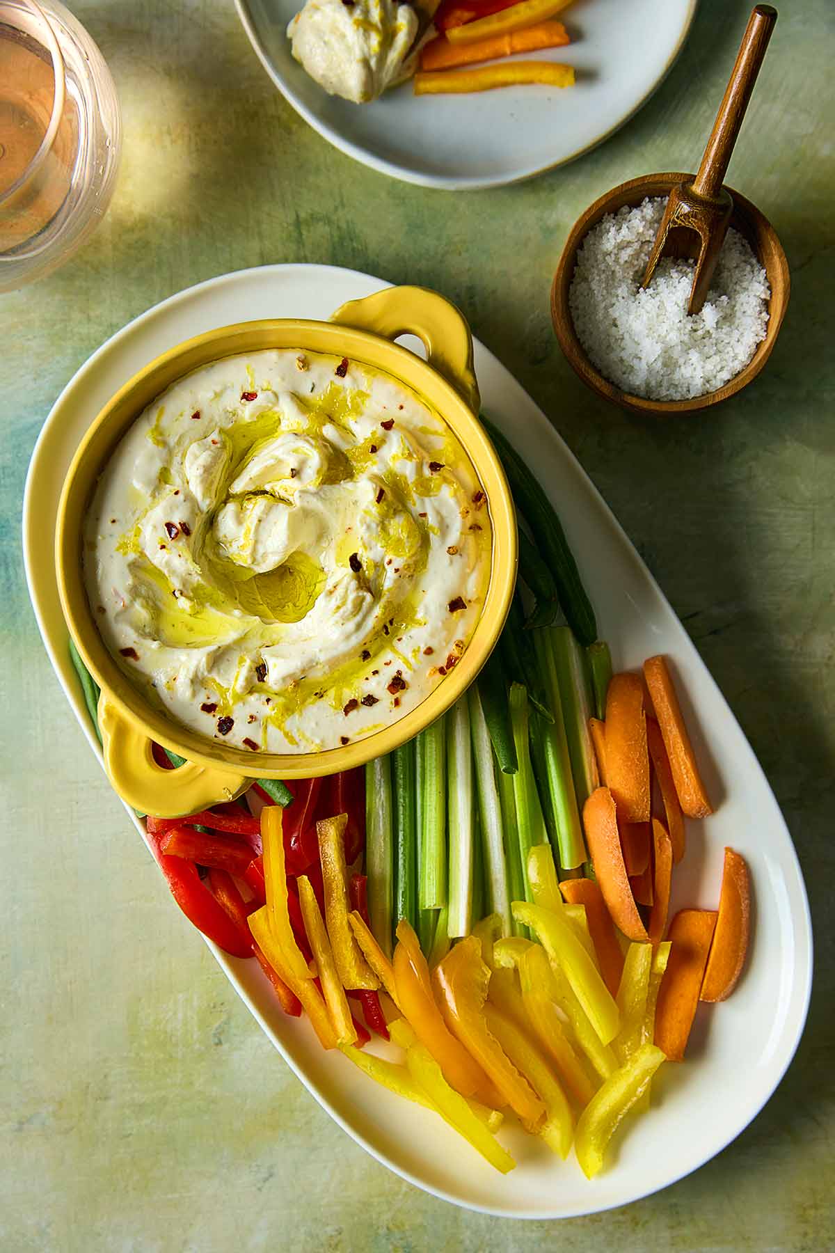 A bowl of whipped feta dip topped with oil and lemon zest on a platter of raw vegetables.