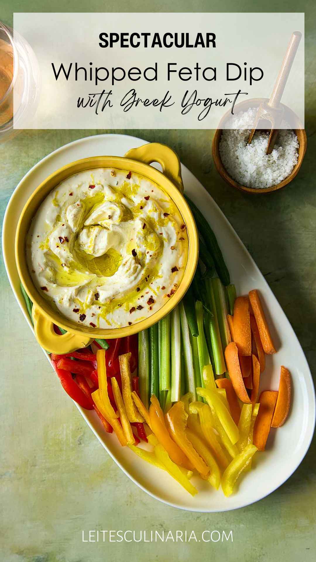 A bowl of whipped feta dip topped with oil and lemon zest on a platter of raw vegetables.